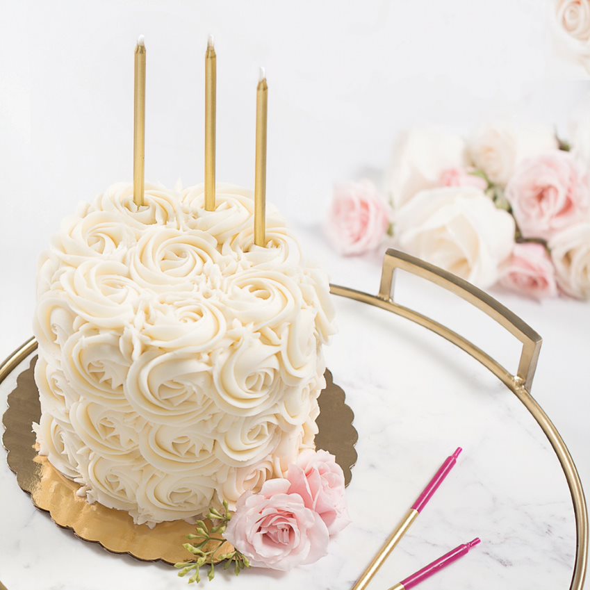 floral cream cake with gold candles surrounded by pink and gold candles