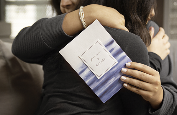 Woman hugging other woman holding sympathy card